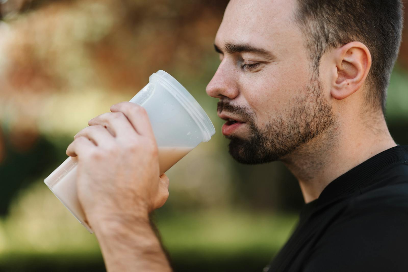 American millenial man in black crew neck tshirt holding a blender cup and sipping his protein shake